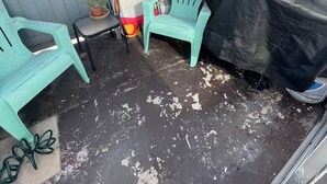 Een klein terras buiten, met een tafel, twee stoelen, een barbecue en een ophangrek voor kleding.