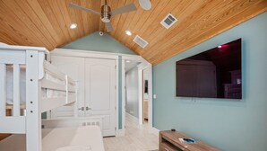 Ein Schlafzimmer mit Etagenbett, Holzboden, einem an der Wand montierten Fernseher und einem Holzschrank.