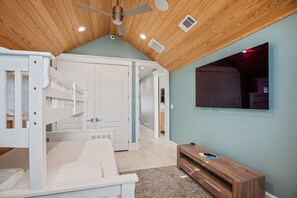 A bedroom with a bunk bed, a wooden ceiling, a TV mounted on the wall, and a wooden cabinet.