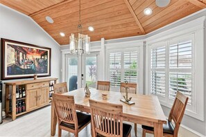 A dining area with a wooden table and chairs, a chandelier, and a painting on the wall.