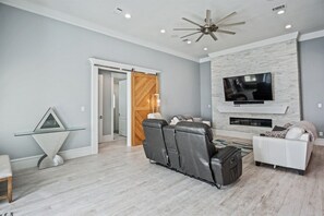 A living room with a fireplace, a TV mounted on the wall, a ceiling fan, and a sectional sofa.