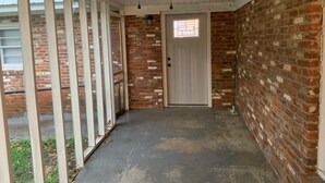 Une véranda couverte avec un ventilateur de plafond, une porte avec une fenêtre et des murs en briques.