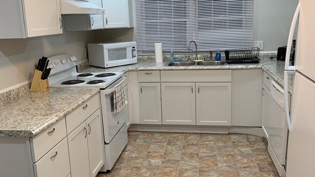 Une cuisine de taille réduite avec des meubles blancs, un four à micro-ondes, une cuisinière et un évier.