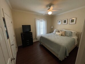 A bedroom with a bed, a television on a dresser, a ceiling fan, and three framed pictures on the wall.