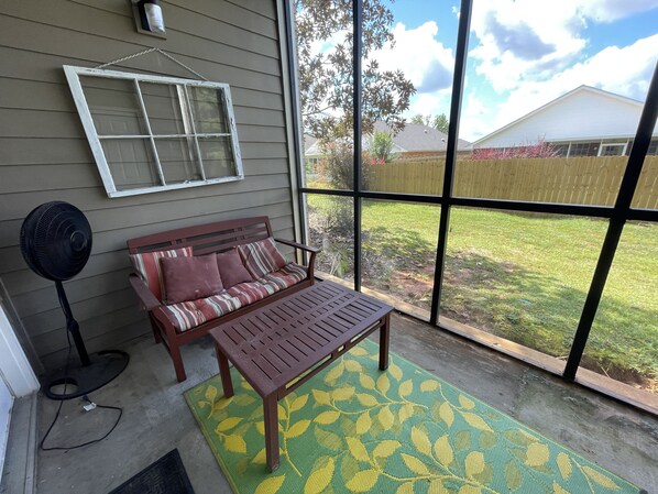 A covered porch with a wooden bench, a small table, and a fan.