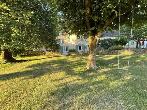 A grassy yard with a swing set and a house with green shutters in the background.