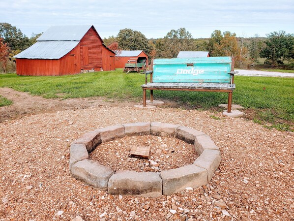 A rural setting with a red barn, a Dodge truck, and a fire pit.