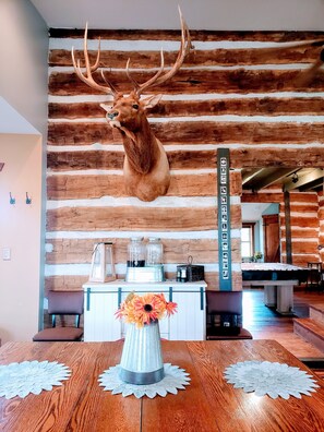 A rustic interior with a mounted deer head on a wooden wall, a dining area with a table, and a bench. - Relaxing Cabin Retreat with Firepit and Large Party Deck (Meta)