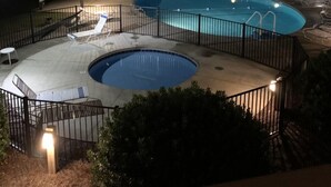 A nighttime view of a swimming pool with a wooden deck and lounge chairs. - Ocean-side condominium with pool and private beach access (Atlantic Beach)