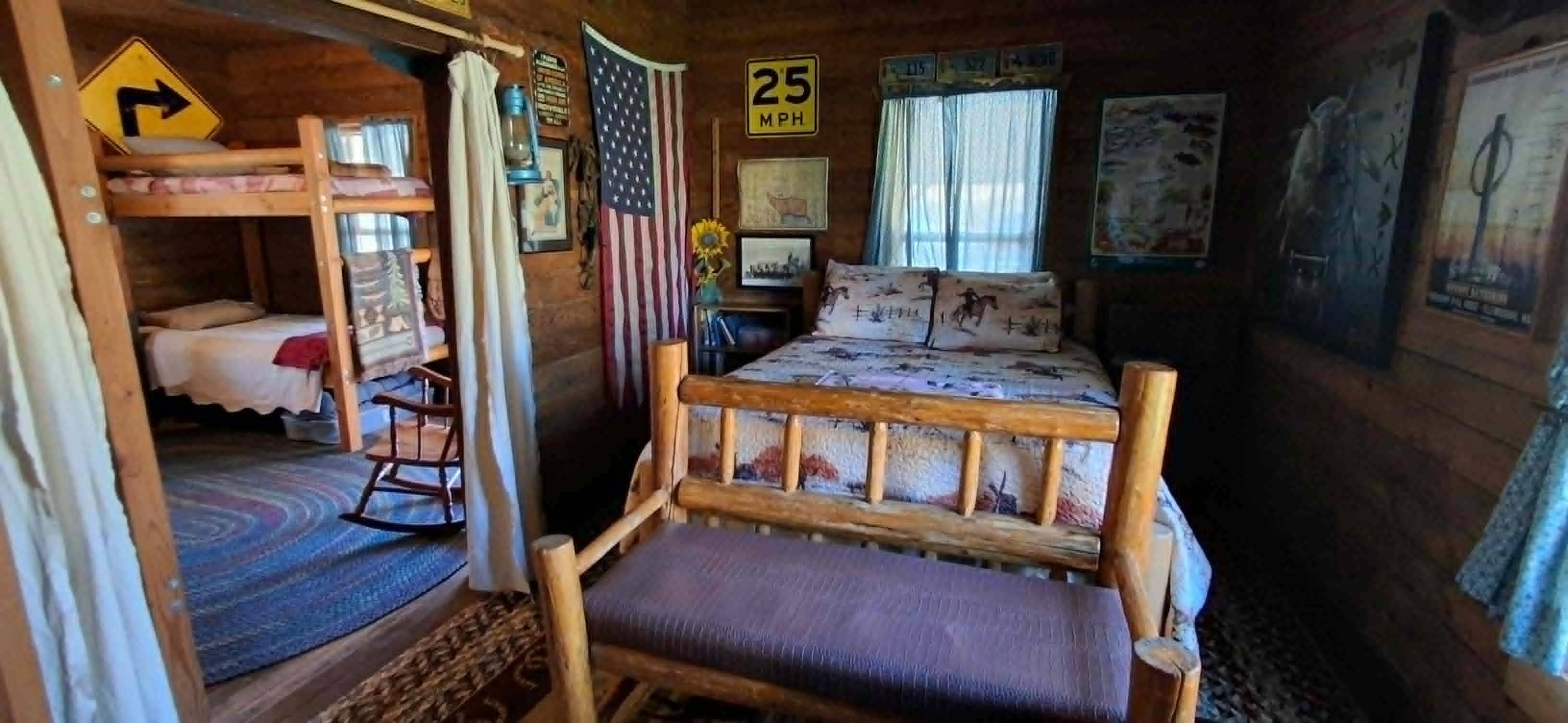 L'interno accogliente di una baita rustica, con un letto a castello, una poltrona a dondolo e un letto con biancheria a motivi decorativi.