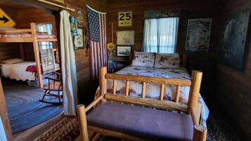 L'interno accogliente di una baita rustica, con un letto a castello, una poltrona a dondolo e un letto con biancheria a motivi decorativi.