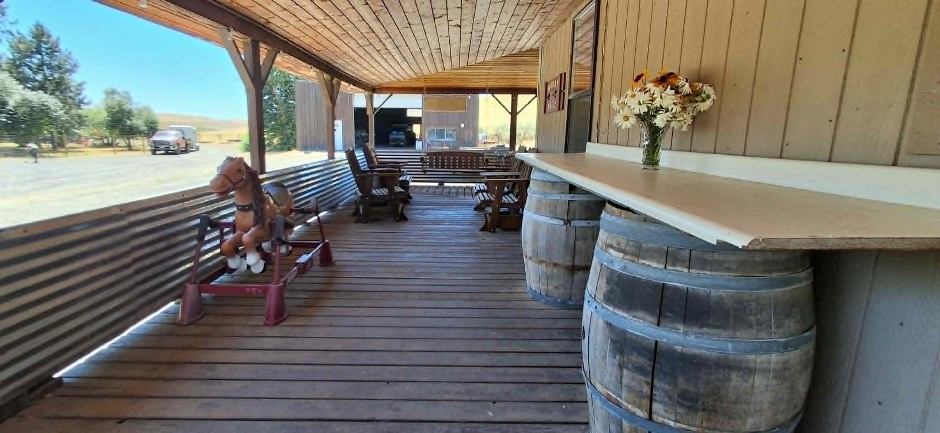 Un espace extérieur abrité, avec des bancs en bois, une table en bois et un vase rempli de fleurs.