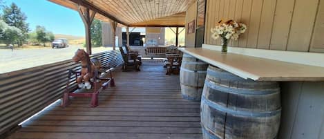 A covered outdoor seating area with wooden benches, a wooden table, and a vase with flowers.