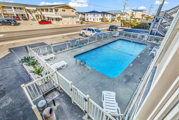 A rectangular pool with a white deck and lounge chairs, surrounded by a white fence.