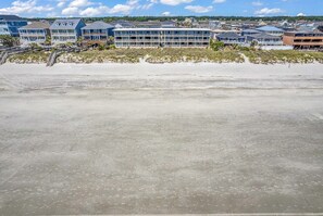 Un hotel frente a la playa con edificios de varios pisos, una playa arenosa en primer plano y un cielo despejado.