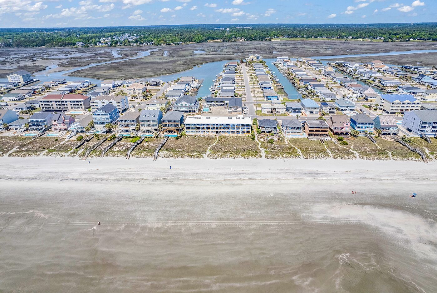 An aerial view of a coastal residential area with houses, a beach, and a marina.