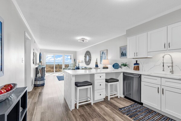 Una cocina moderna con armarios blancos, una isla central con taburetes y vistas al exterior.