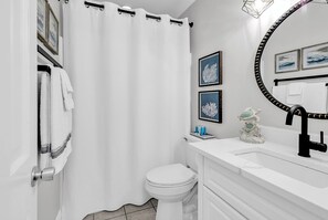 Un baño moderno con inodoro blanco, un lavamanos blanco con grifo negro, cortina de ducha blanca y cuadros en la pared.