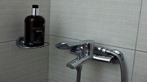 A bathroom with a black liquid soap dispenser and a chrome shower head.
