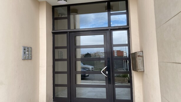 A modern entrance with a glass door and a metal intercom system.