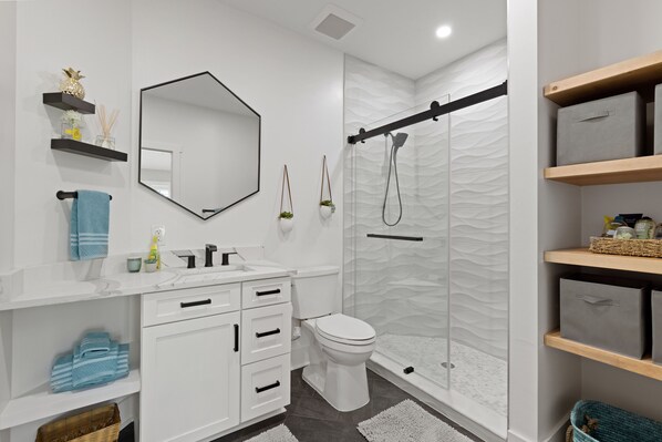 A modern bathroom with a white vanity, a toilet, a shower with a glass door, and built-in shelves.