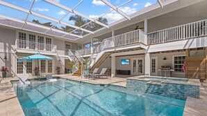 Uma grande piscina interior com teto de vidro, vários níveis com varandas e uma área à beira da piscina com espreguiçadeiras e um guarda-sol.