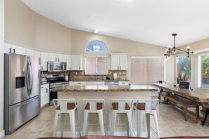 A modern kitchen with white cabinets, stainless steel appliances, a granite countertop, and a central island with bar stools.