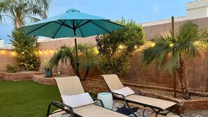 A patio area with two lounge chairs, a large umbrella, and a small table. - On HGTV Show House Hunters! Heated Pool! Family & Dog friendly, Prime location!  (Gilbert)