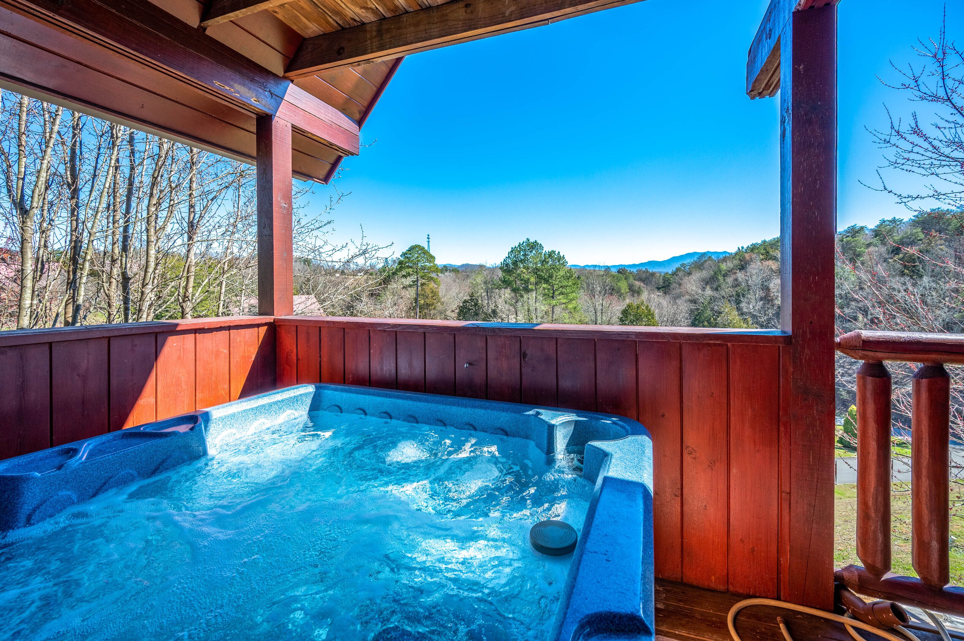 Een hottub op een houten terras, met uitzicht op bomen en bergen.