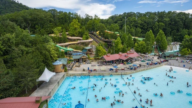 Una grande piscina all'aperto circondata da alberi, con uno scivolo e un'area relax coperta.