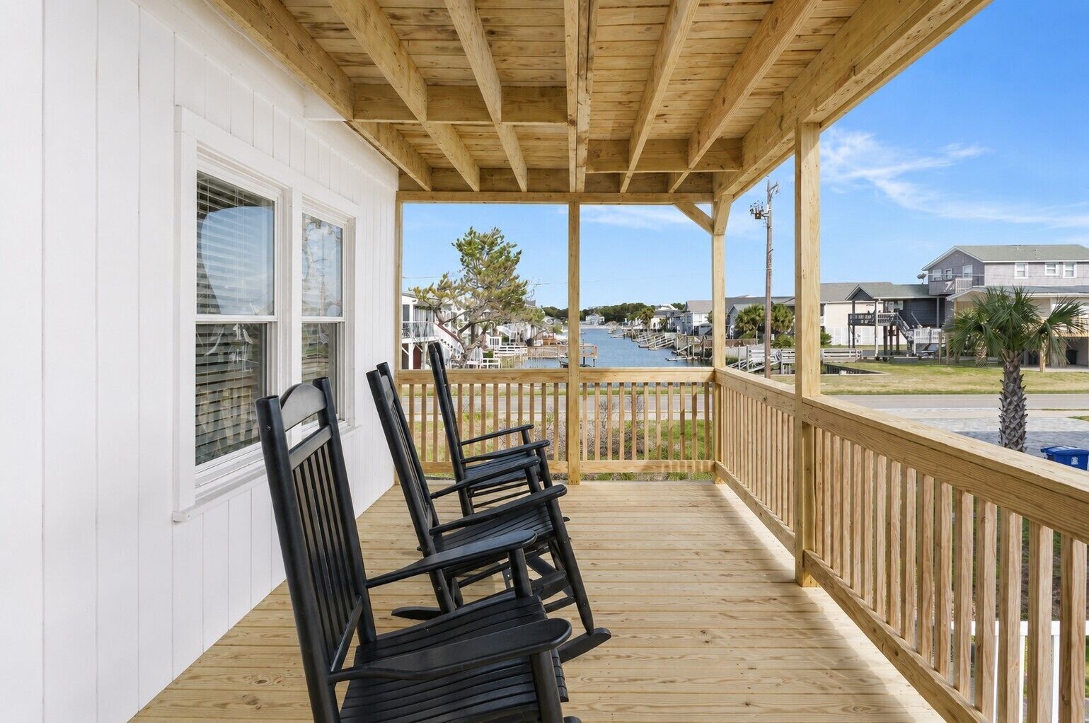 Une véranda couverte avec des balustrades en bois, une vue sur un port de plaisance et un ciel dégagé.