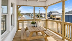 A covered deck with a wooden table and benches, overlooking a marina and residential buildings. - 8BR/6Ba House, Private Pool, Minute Walk To Beach, Dog Friendly, Sleeps 24 (North Myrtle Beach)