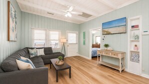 A living room with a sectional sofa, a coffee table, a wooden floor, a ceiling fan, and a view of the beach through a window. - 8BR/6Ba House, Private Pool, Minute Walk To Beach, Dog Friendly, Sleeps 24 (North Myrtle Beach)