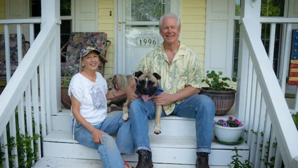 A porch with a white railing, a dog, and a person sitting on the steps.