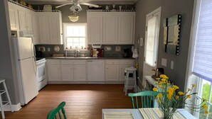 A kitchen with white cabinets, a wooden floor, a dining table with striped placemats, and a vase with yellow flowers.