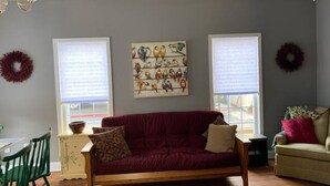 A living room with a wooden sofa, two windows with blinds, a chandelier, and wall art.