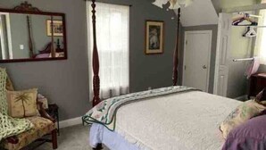 A bedroom with a four-poster bed, a chair, a mirror, and a door.