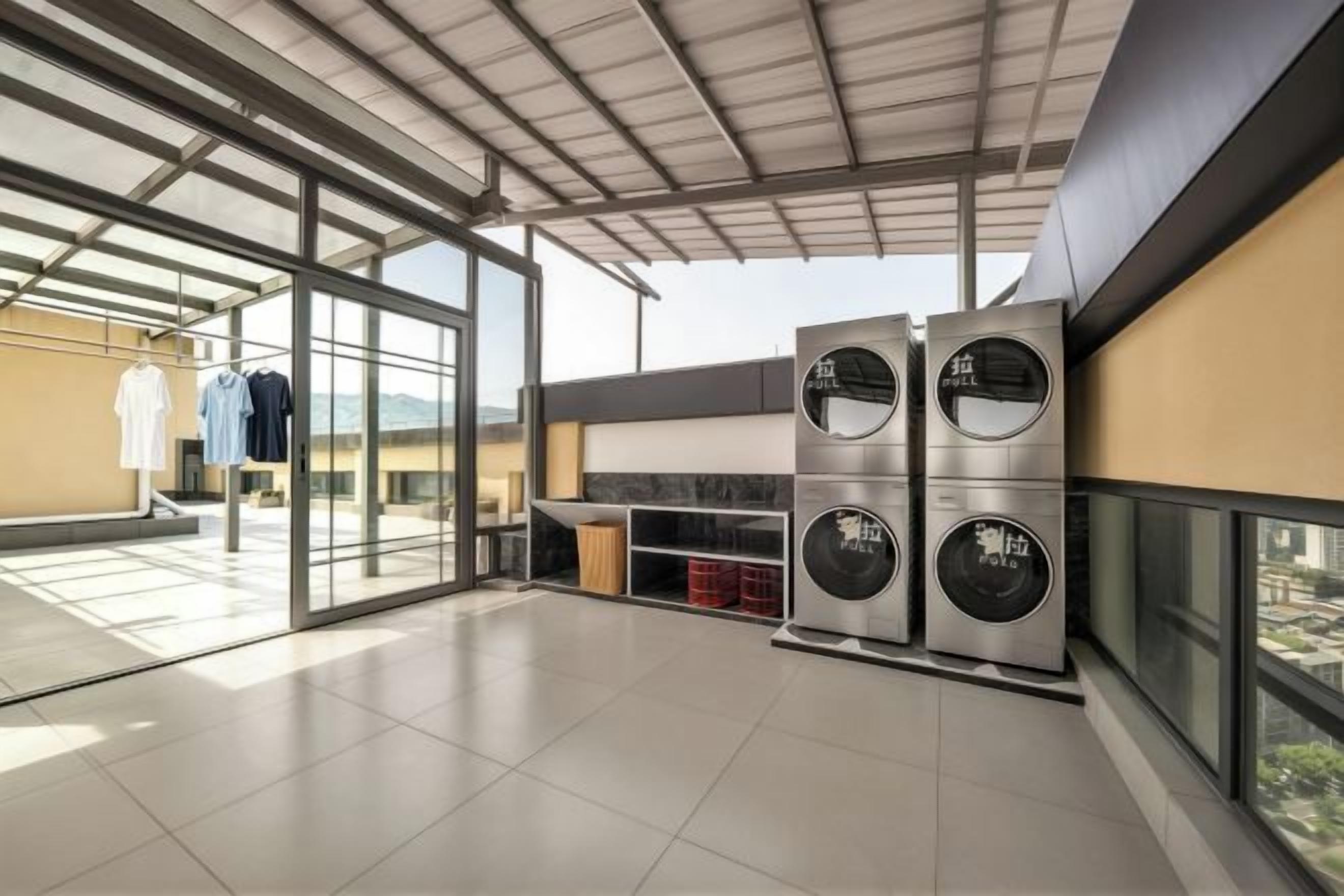 A modern kitchen with a glass door leading to a balcony, a large industrial-style washing machine, and a view of the cityscape.