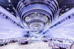 Een ruime balzaal met een centraal, rond hanglamp, meerdere ronde tafels en een modern plafondontwerp.
