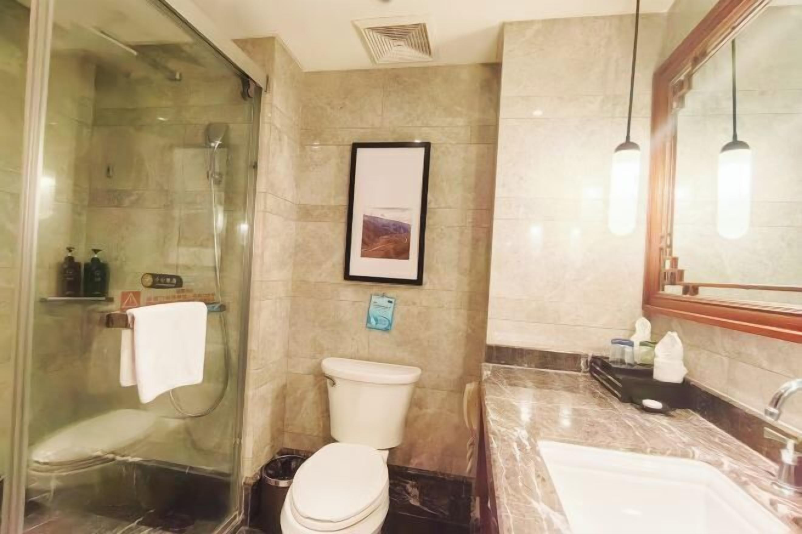 A bathroom with a glass-enclosed shower, a toilet, a sink, and a framed picture on the wall.