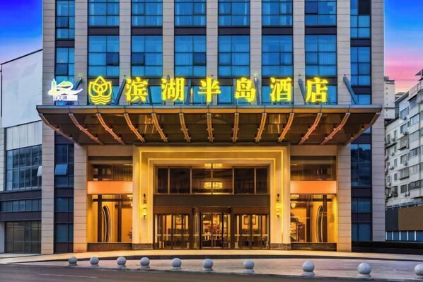 A hotel entrance with a modern facade, large glass windows, and a prominent sign in a foreign language. - Binhu Peninsula Hotel (Chongqing)