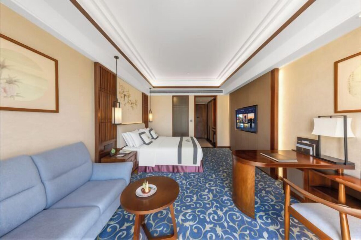 A hotel room with a bed, a sofa, a desk, and a TV.