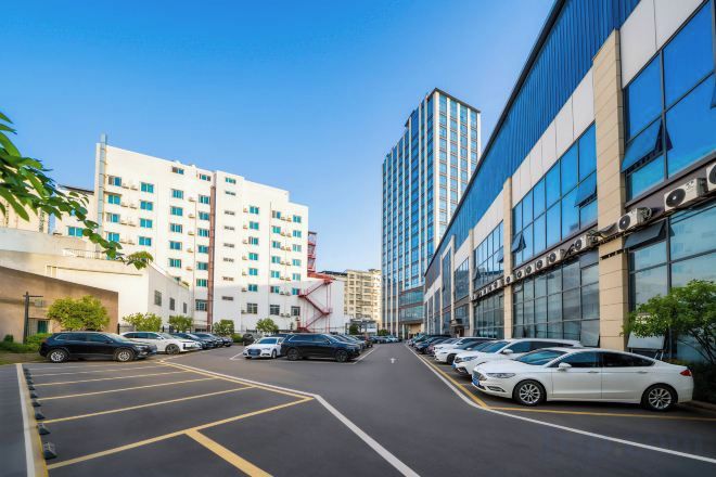 A parking lot with multiple cars, a building with large windows, and a tall structure in the background.