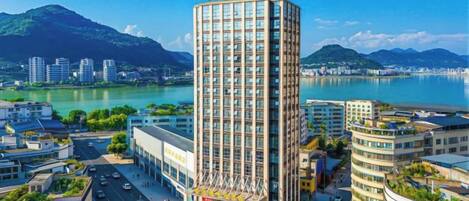 A high-rise hotel with a modern design, located near a body of water and mountains.