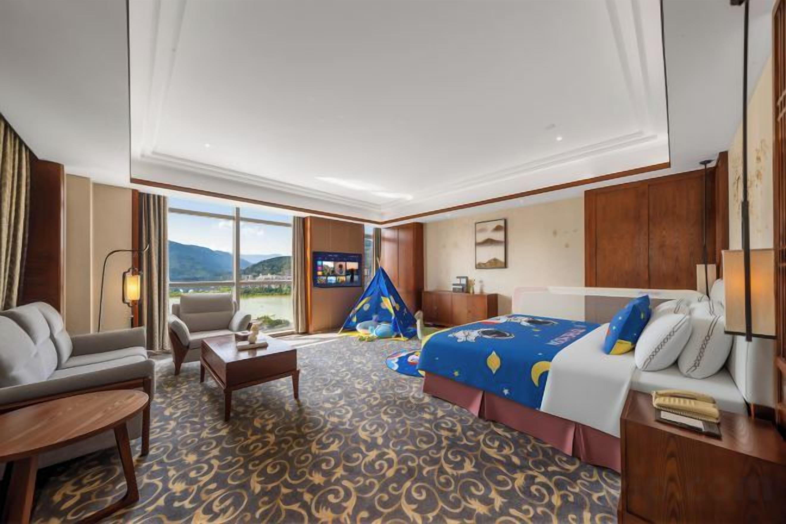 A hotel room with a bed, a sofa, a desk, and a view of the outdoors.