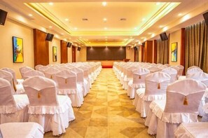 Un salón de conferencias con filas de sillas y mesas blancas, un escenario al frente y un suelo a cuadros.
