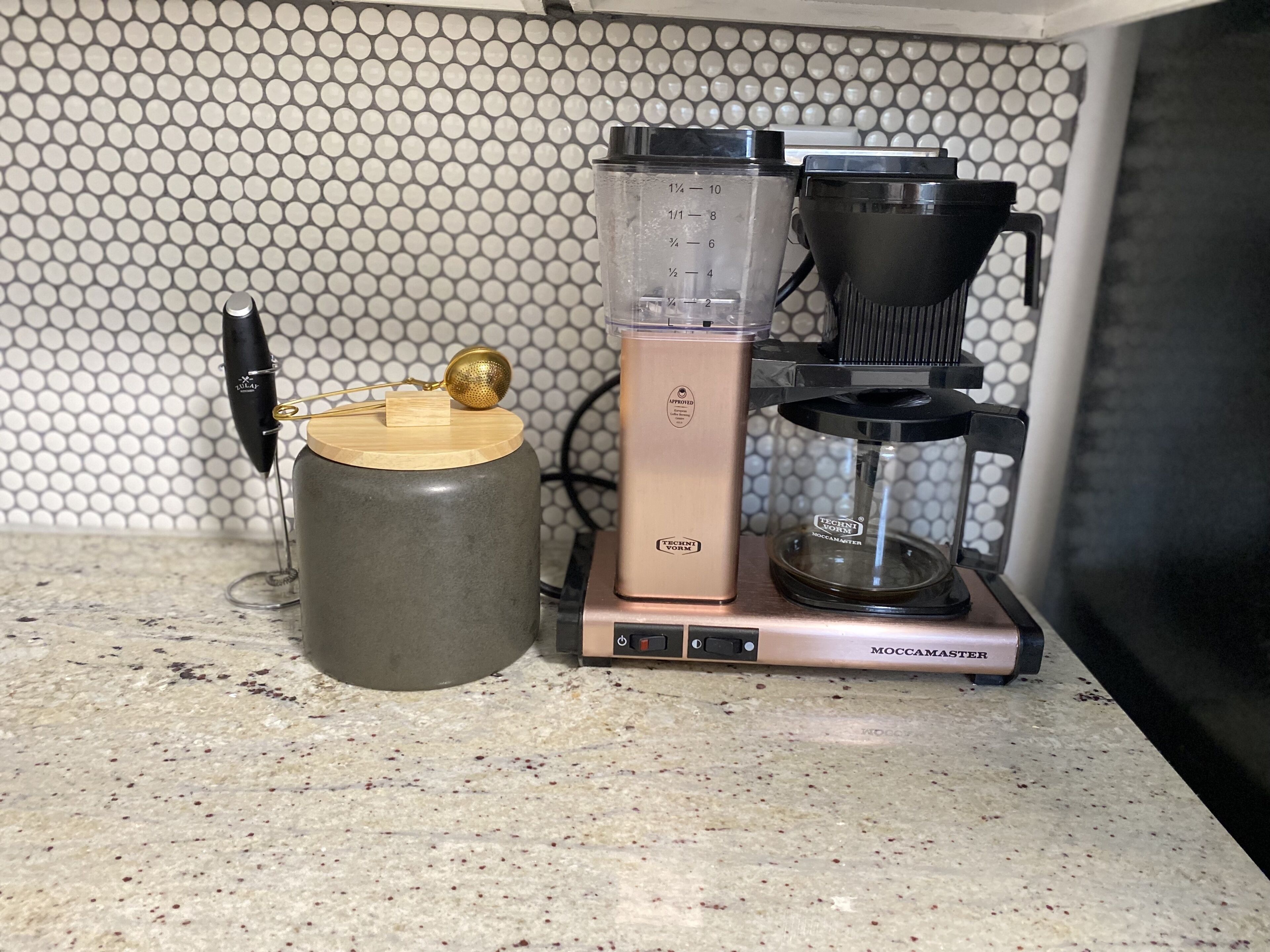Eine Küche mit einer Kaffeemaschine, einer Waage und einem Behälter auf einer Arbeitsplatte.