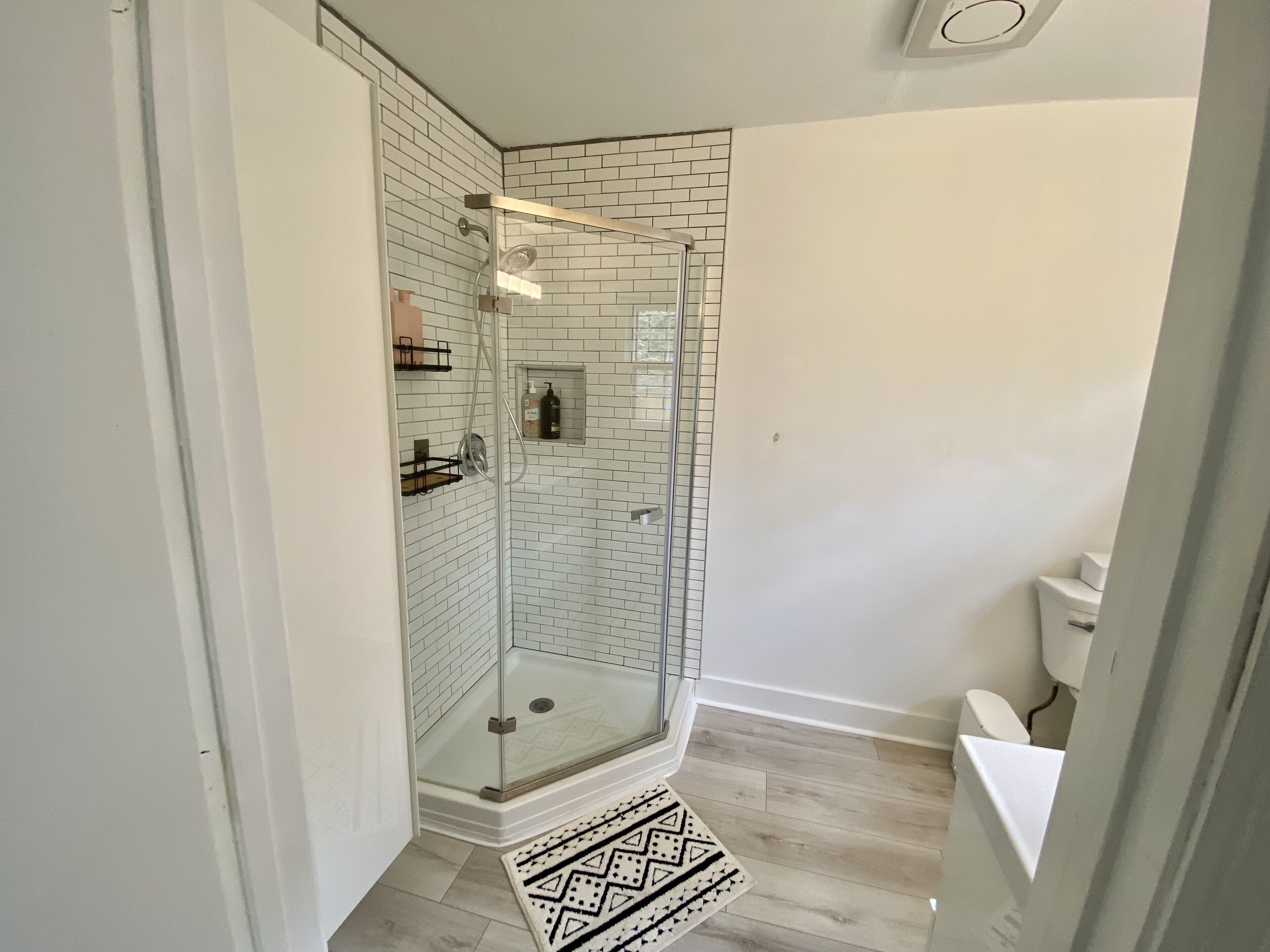 Un baño moderno con ducha de vidrio, paredes de azulejos blancos y suelo de madera.
