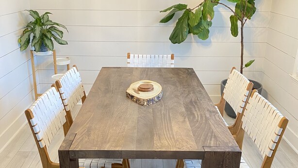 Un coin repas avec une table en bois et six chaises, un luminaire suspendu et deux plantes en pot.