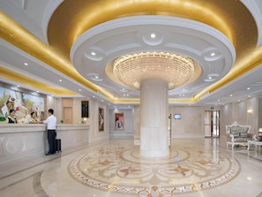 Um saguão de hotel com uma coluna central, balcão de recepção e um candelabro.